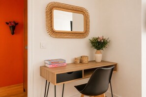 Une pièce avec un bureau en bois, une chaise noire, un miroir avec un cadre en osier et un vase rempli de fleurs.