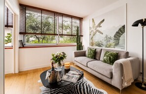 A living room with a sofa, a coffee table with a vase, a cactus, and a framed picture on the wall. - Lavie Maison | Eiffel Nearby - Beaugrenelle (Paris)