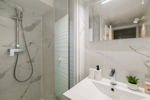 A modern bathroom with a glass shower enclosure, a white sink with a plant, and a mirror reflecting the room. - Lavie Maison Cozy Flat in Parisian Passage (Paris)