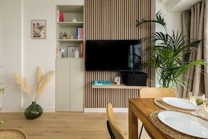 A dining area with a wooden table, chairs, and a television mounted on a wall with a slatted design. - Lavie Maison Cozy Flat in Parisian Passage (Paris)