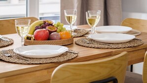 Una mesa de comedor dispuesta con platos, cubiertos y una cesta de frutas.