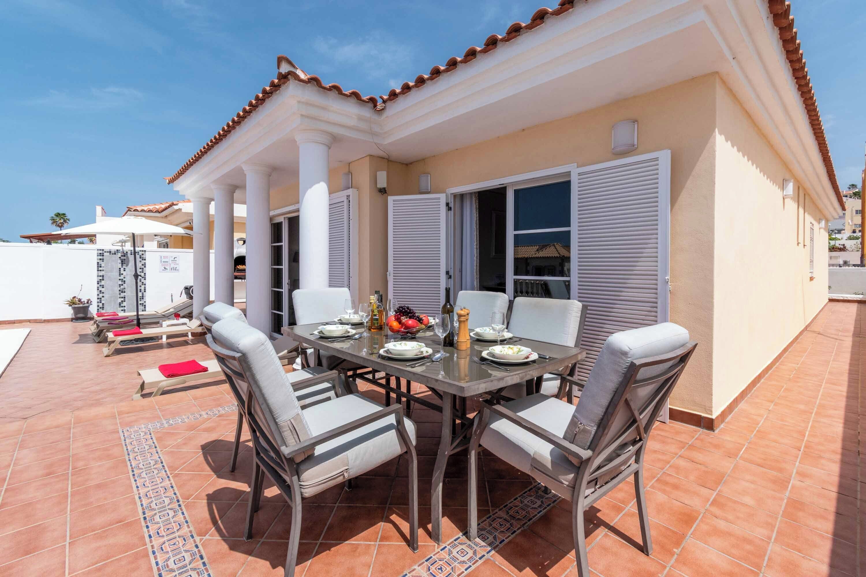 A dining area with a table set for four, surrounded by chairs, and a view of a building with a tiled roof.