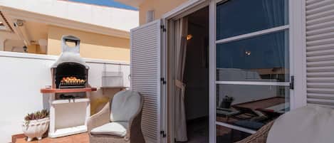 Un patio con una parrilla, mobiliario de mimbre y una puerta corrediza de vidrio que da a un espacio interior.