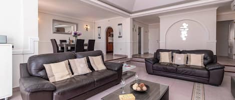 A spacious living area with two dark leather sofas, a glass coffee table, and a dining area in the background.