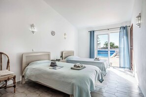 Ein Hotelzimmer mit zwei Betten, einem Sessel, einem kleinen Tisch und Blick auf einen Swimmingpool.