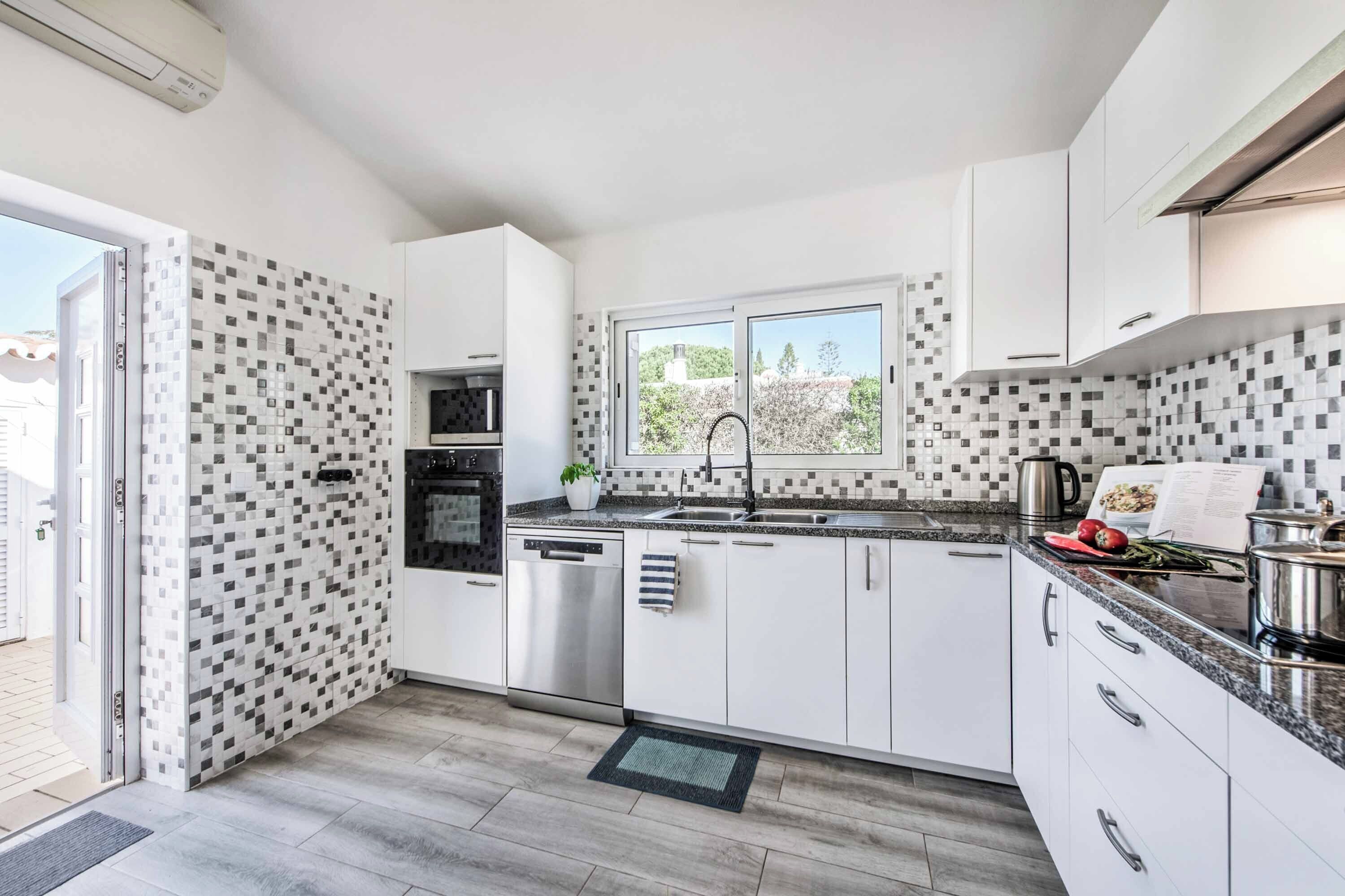 Una cocina moderna con armarios blancos, lavavajillas de acero inoxidable y una ventana con vista a vegetación.