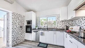 Een moderne keuken met witte kasten, een roestvrijstalen vaatwasser en een raam met uitzicht op groen.