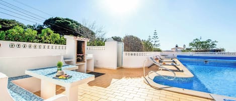 A poolside area with a tiled deck, lounge chairs, and a small table with a plant.