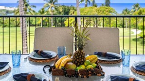 Mesa lista para comer con un arreglo de frutas tropicales, una piña como centro de mesa, y vista al océano y al campo de golf.