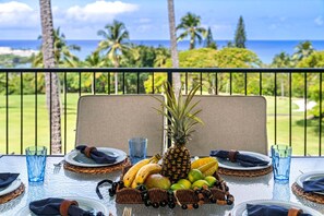 Ein Esstisch, gedeckt für ein Essen, mit einer tropischen Obstkomposition und einer Ananas als Mittelpunkt, mit Blick auf den Ozean und den Golfplatz.