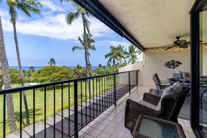 Ein Balkon mit Korbmöbeln, einem Deckenventilator und Blick auf das Meer und Palmen.
