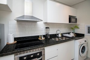 Een moderne keuken met witte kasten, een zwart aanrecht, een fornuis, een magnetron en een wasmachine.