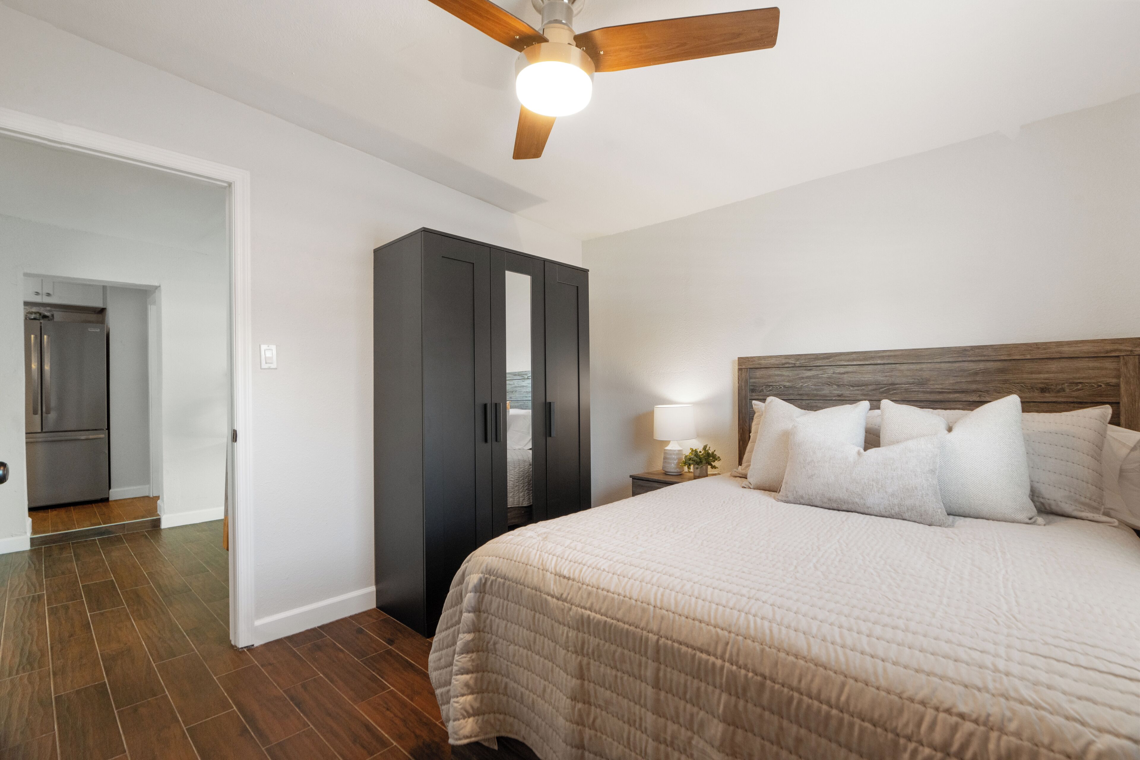 A bedroom with a bed, a nightstand, a lamp, a wardrobe, and a ceiling fan.