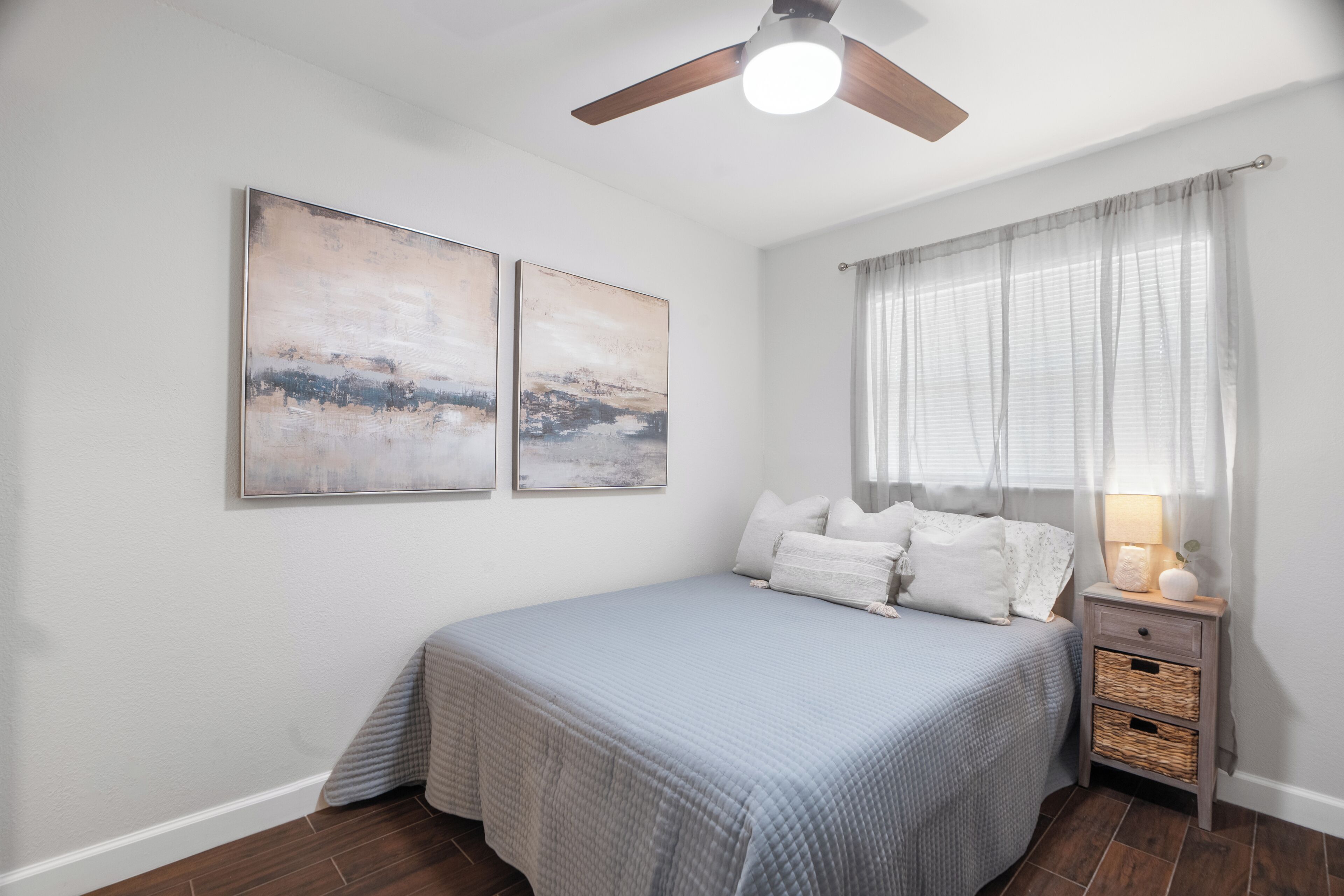 A bedroom with a bed, a nightstand, a lamp, and two wall-mounted paintings.