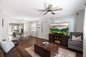 Ein modernes Wohnzimmer mit Flachbildfernseher, Deckenventilator und Essbereich mit einer Kristallleuchtre.