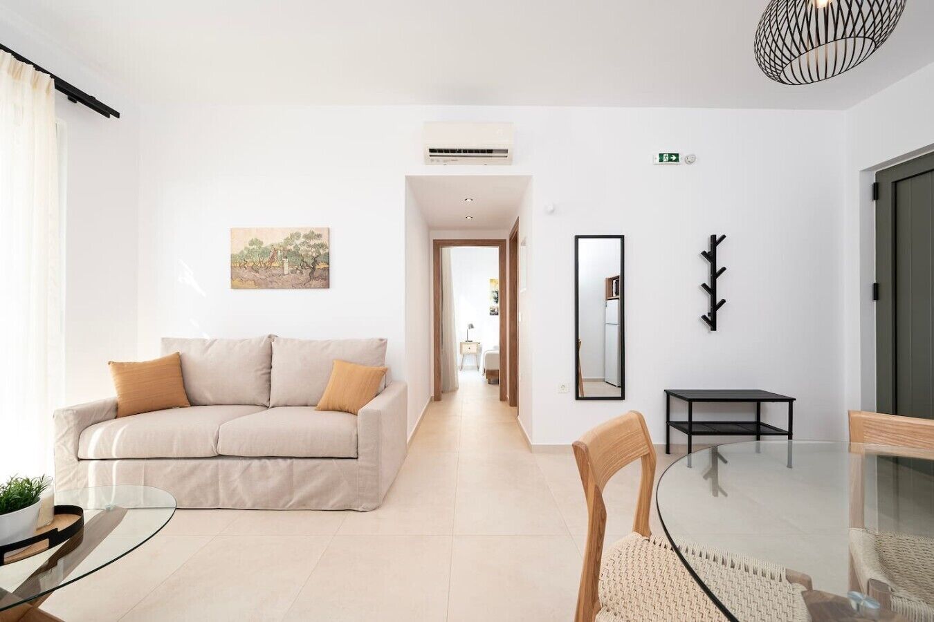 A modern hotel room with a sofa, a dining table, a chair, a mirror, and a coat rack.