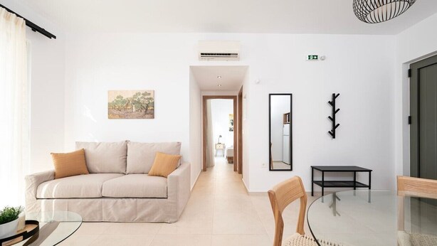 Ein modernes Hotelzimmer mit Sofa, Esstisch, Stuhl, Spiegel und Garderobe.