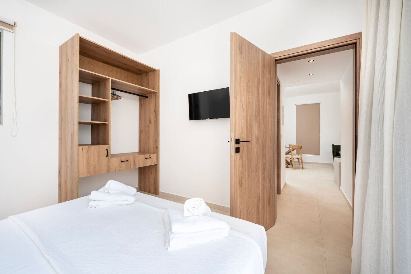 Una habitación de hotel con una cama, un armario de madera, un televisor y una puerta abierta que da a otra habitación.