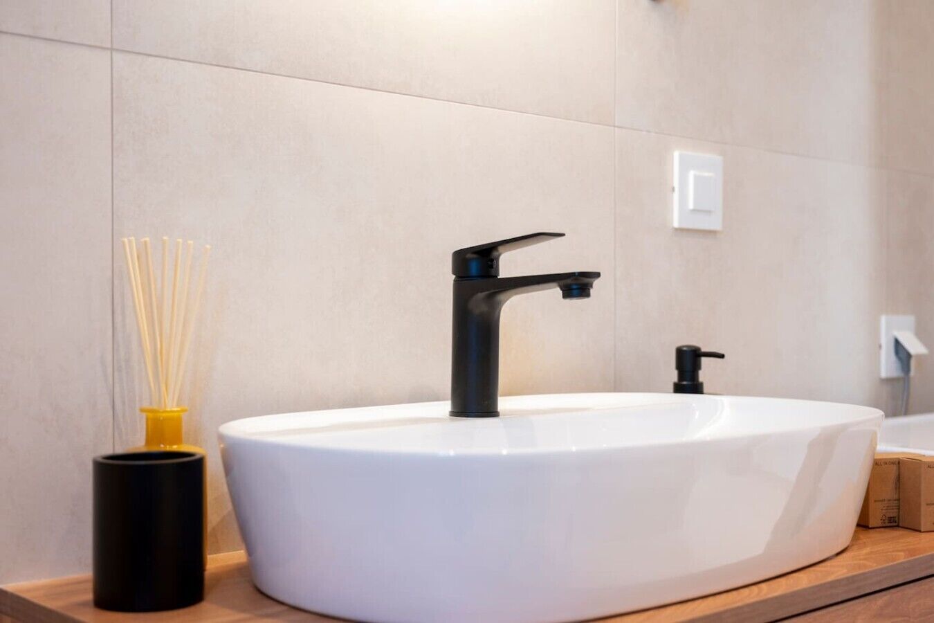 Un baño moderno con un lavamanos blanco independiente, grifo negro y un portavelas amarillo y negro.