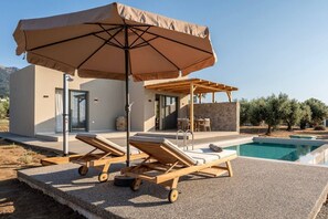 Ein moderner Poolbereich im Freien mit Liegestühlen, einer Pergola und einem großen Sonnenschirm.