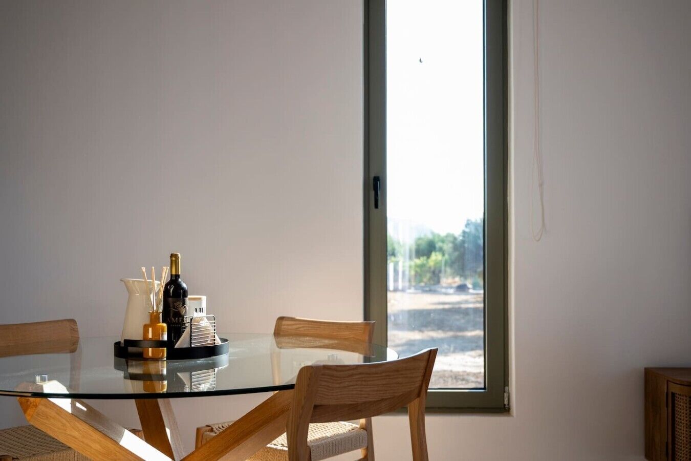 A dining table with chairs, a glass top, and a bottle of wine.