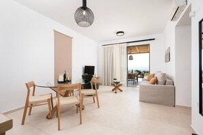 Ein modernes Wohnzimmer mit einem Glastisch, Holzsesseln, einer Couch und Blick durch ein großes Fenster.