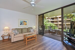 Ein Zimmer mit einer Couch, einem Couchtisch, einem Deckenventilator und Blick auf ein Gebäude mit Balkonen.