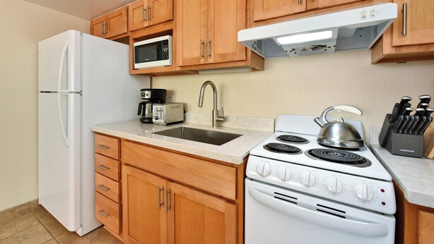 A compact kitchen with wooden cabinets, a white refrigerator, a microwave, a toaster, a sink, and a stove. - Sweet Studio with AC (Lahaina)