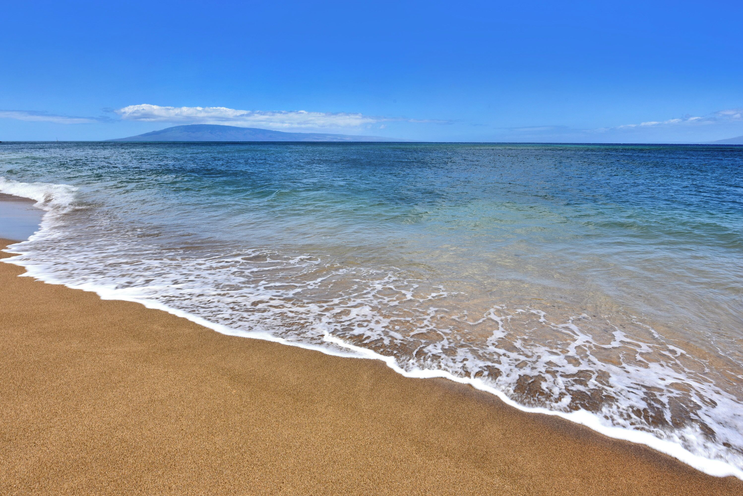 A beach with clear water and a distant mountain.
