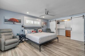 Ein Schlafzimmer mit einem Bett, zwei Stühlen, einem Kleiderschrank und einem Deckenventilator.