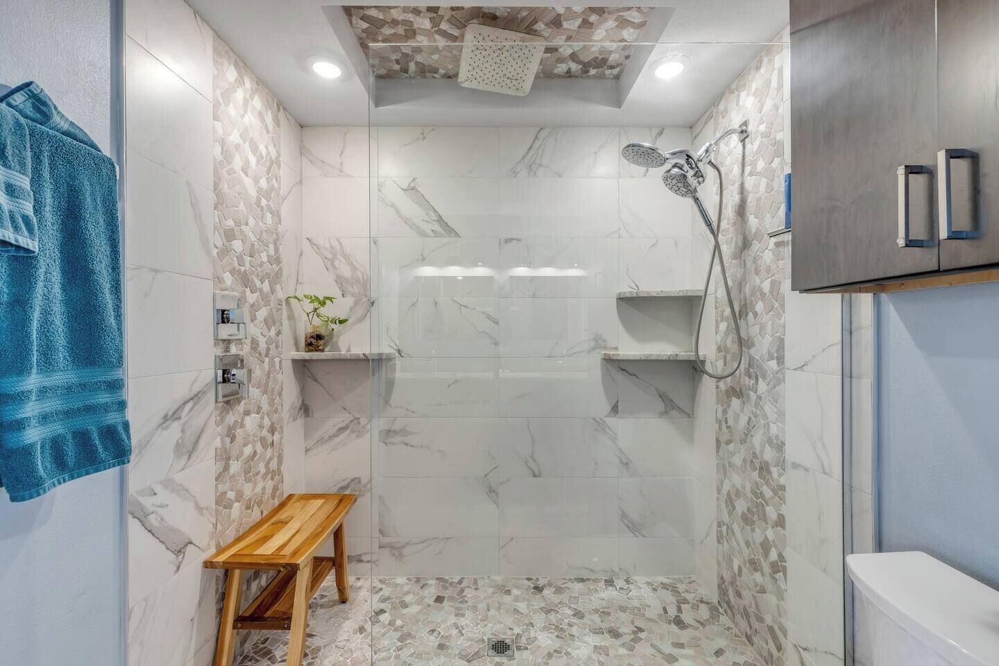 A bathroom with a shower, marble walls, a wooden bench, and a towel rack.