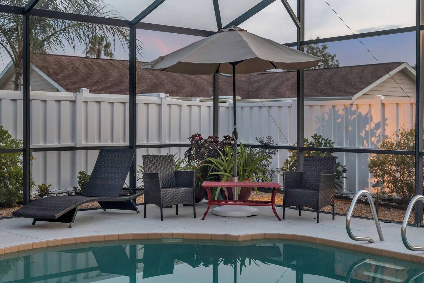 Un espace aménagé au bord de la piscine, doté d’une structure en verre, de deux chaises longues, d’une table ornée de plantes en pot et d’une piscine.