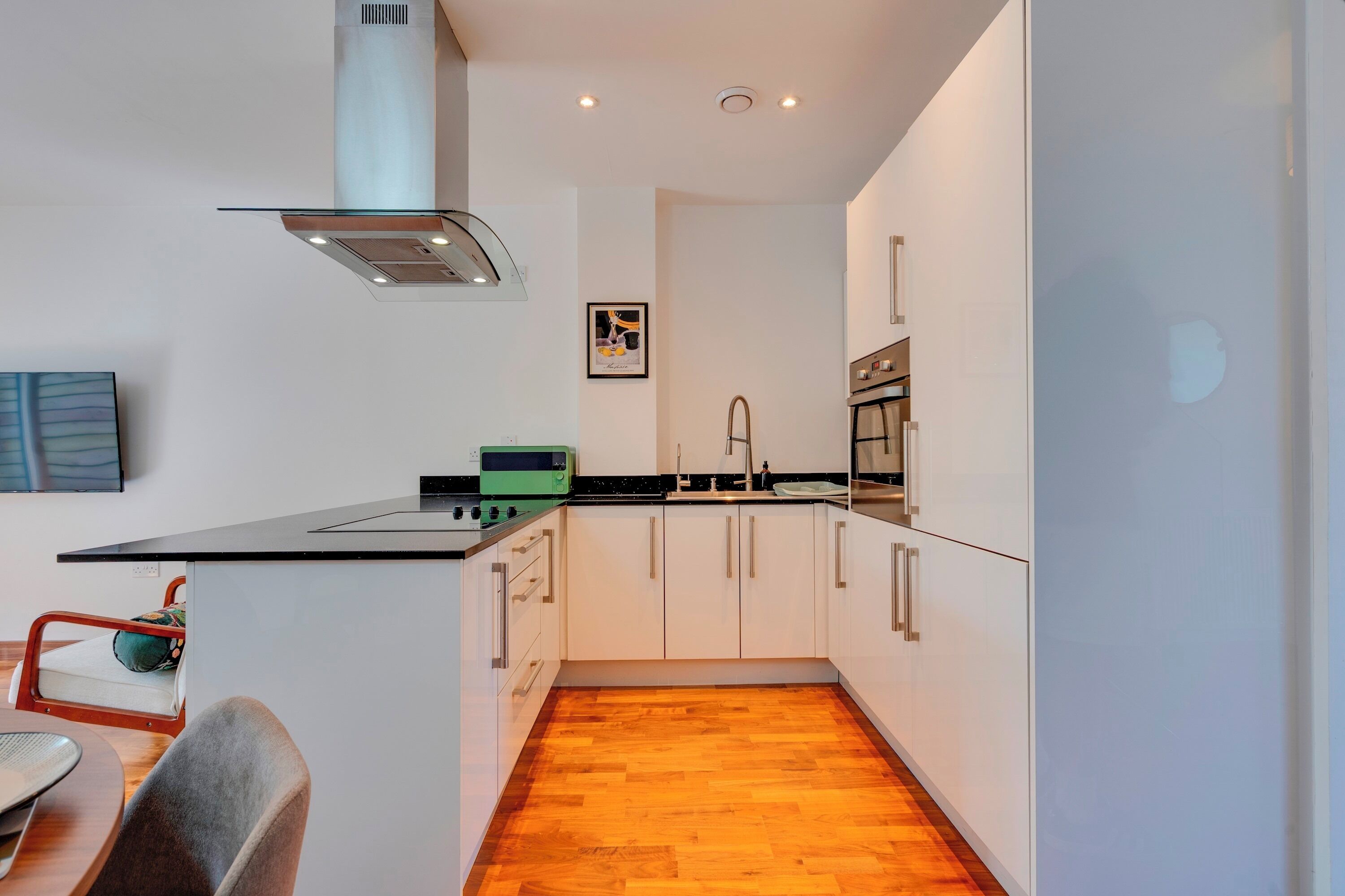 A modern kitchen with white cabinets, a black countertop, and a wooden floor.