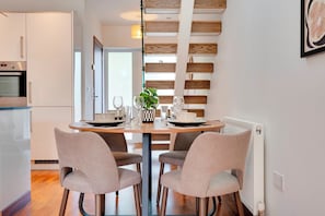 Une cuisine moderne dotée d’un four encastré et d’un coin repas avec deux chaises et une table préparée pour deux personnes.