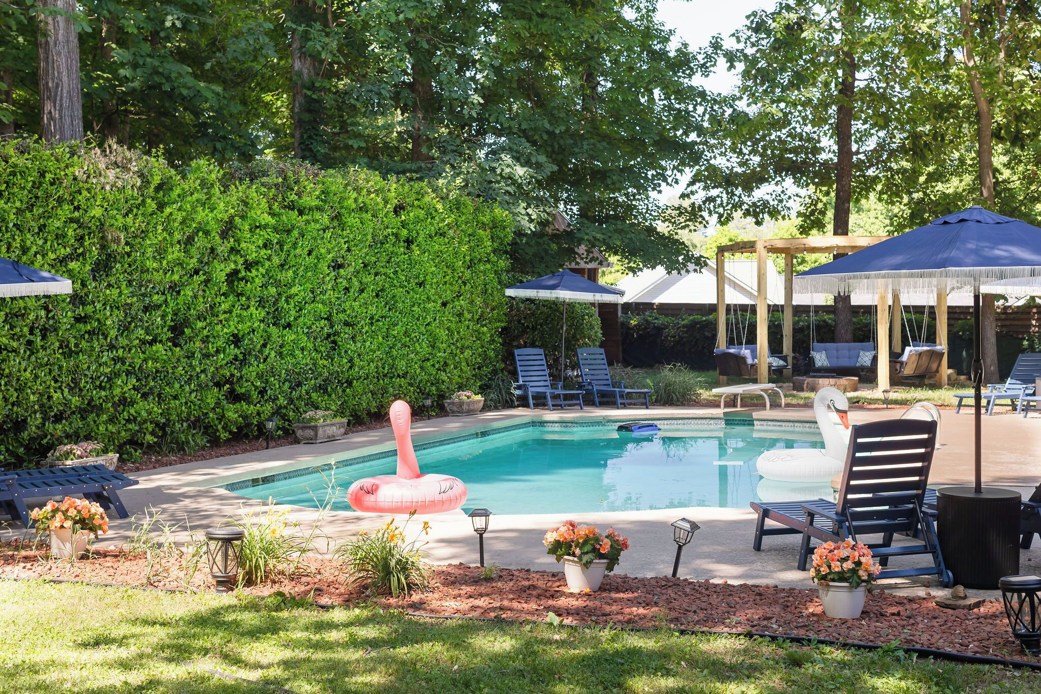 A swimming pool with lounge chairs and umbrellas, surrounded by greenery.
