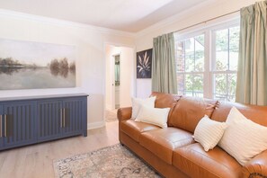 Ein Wohnzimmer mit braunem Ledersofa, einem blauen Schrank, einem Gemälde an der Wand und Blick durch ein Fenster.