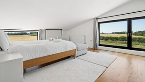 A modern bedroom with a large bed, a sofa, and a view of a field through a sliding door. - Secluded, contemporary barn in expansive gardens - Pass the Keys (Wantage)