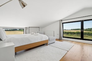 A modern bedroom with a large bed, a sofa, and a view of a field through a sliding door. - Secluded, contemporary barn in expansive gardens - Pass the Keys (Wantage)