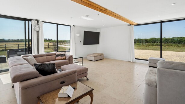 A spacious living room with a large sofa, a coffee table, and a television mounted on the wall. - Secluded, contemporary barn in expansive gardens - Pass the Keys (Wantage)