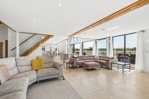 A spacious living room with a large sectional sofa, a coffee table, and a dining area with chairs. - Secluded, contemporary barn in expansive gardens - Pass the Keys (Wantage)