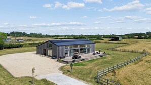 A modern farmhouse with a large open patio area, surrounded by a fenced property. - Secluded, contemporary barn in expansive gardens - Pass the Keys (Wantage)