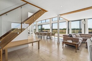 A spacious living area with a modern staircase, a dining table with chairs, and a large window offering a view of the outdoors.