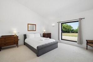 A bedroom with a large bed, a dresser, a nightstand, a mirror, and a window with a view of greenery. - Secluded, contemporary barn in expansive gardens - Pass the Keys (Wantage)