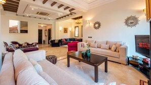 A spacious living room with a large sofa, a coffee table, and a television. - 3 BDRM Villa Garden & Pool Front (Marrakech)