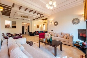 A spacious living room with a large sofa, a coffee table, and a television. - 3 BDRM Villa Garden & Pool Front (Marrakech)