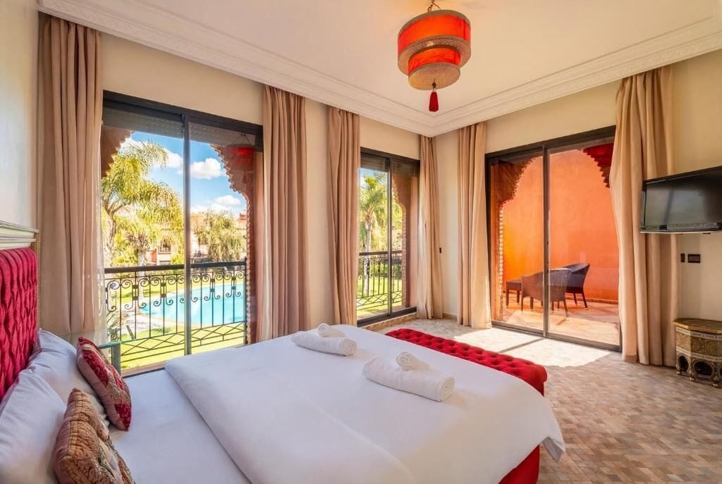 Habitación de hotel con una cama grande, televisión y balcón con vista a la piscina.
