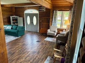 Ein Innenraum einer Blockhütte mit einem grünen Sofa, einem beigefarbenen Sessel und einem Holzboden.