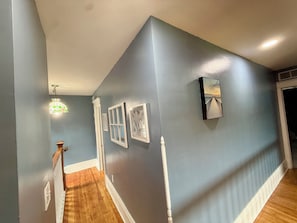 A hallway with a wooden floor, a staircase, and a wall with framed pictures and a mirror. - Your Lake Escape Starts at Balti Bay Lodge New Baltimore 3 bedroom, Boat Parking (New Baltimore)