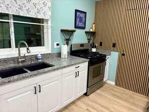 Uma cozinha com bancada de granito, eletrodomésticos de aço inoxidável, armários brancos e painel de parede de madeira.