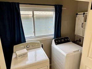 A laundry room with a front-loading washer and dryer, a window with blinds, and a sign indicating the room's purpose. - Your Lake Escape Starts at Balti Bay Lodge New Baltimore 3 bedroom, Boat Parking (New Baltimore)